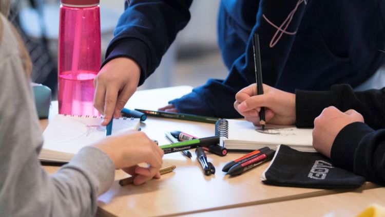 Bildet viser hendene til barn som er i et klasserom. De jobber med oppgaver på et ark.