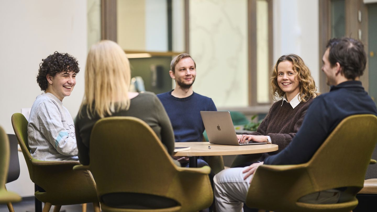 Bildet viser flere kolleger rundt et bord som prater og smiler